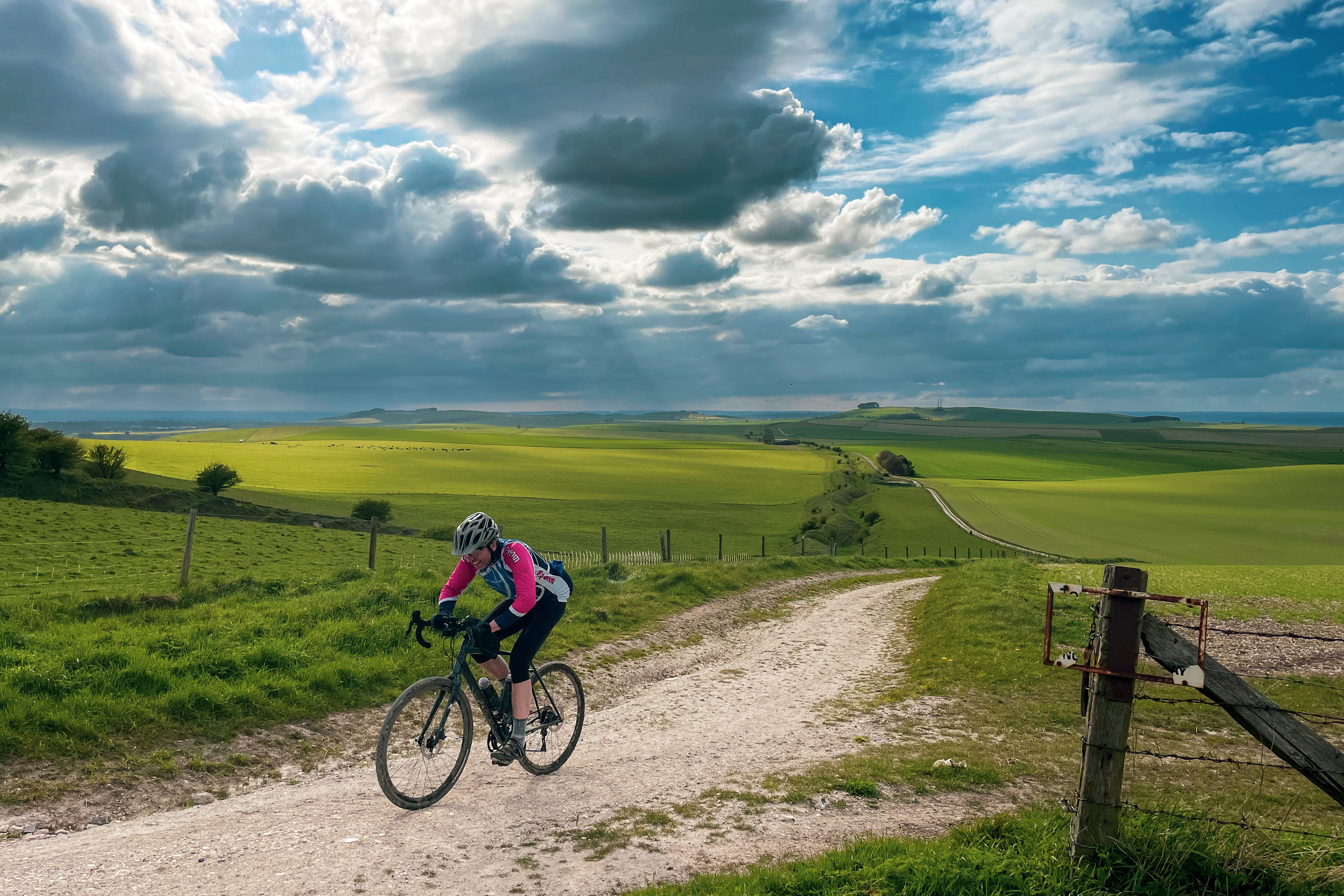 Cyclist climbing chalk track in open downland under dramatic cloudy sky
